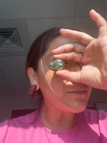 Reviewer holds a polished, iridescent Labradorite crystal over their eye.