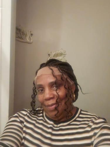 A reviewer wearing a braided wig with curly pieces framing their face.