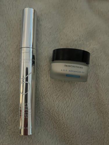 Reviewer's ZO Growth Factor Eye Serum in a sleek silver tube, pictured next to a small jar of eye cream on a soft, grey surface.
