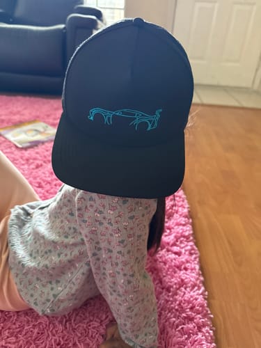 A person wearing the black 80Eighty® Limited Edition DCG87 Hat, showing the light blue embroidered car outline on the front.