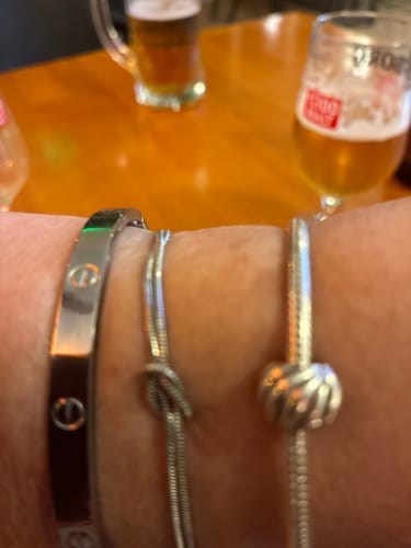 Reviewer's close-up of the silver knot bracelet on a wrist, next to two other bracelets.