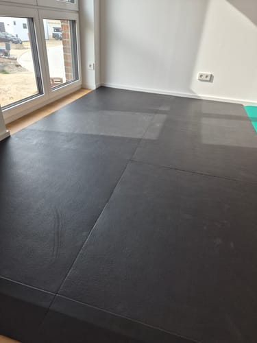 Kunde zeigt die verlegten MaxProtect Bodenschutzmatten auf dem Boden eines leeren Raumes.