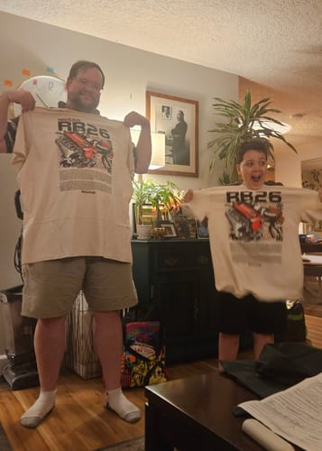 Customer and a child excitedly holding up their matching cream TWIN-TURBO TEE shirts.