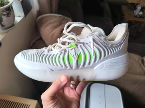 A customer holds up their white and neon green Joker 2 GT 'MIRO' shoe, showing its side profile and unique design.