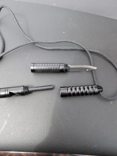 Reviewer's black MultiTool Whistle disassembled on a surface, showing the knife blade, fire starter, and whistle components.