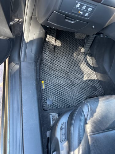 Recenzent pokazuje czarny, dopasowany dywanik samochodowy zainstalowany po stronie kierowcy.