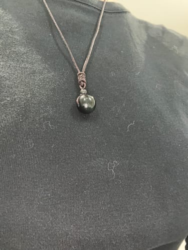 Un client portant le Collier Obsidienne Oeil Céleste avec son pendentif en pierre ronde et noire sur un t-shirt.