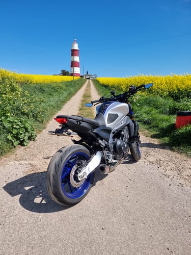 Customer's Universal Adjustable Bracket fitted to their motorcycle on a scenic path with a lighthouse.