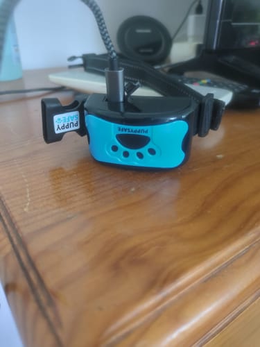 Avis d'un client sur le collier anti-aboiement PuppySafe bleu et noir, branché pour être rechargé sur une table en bois.