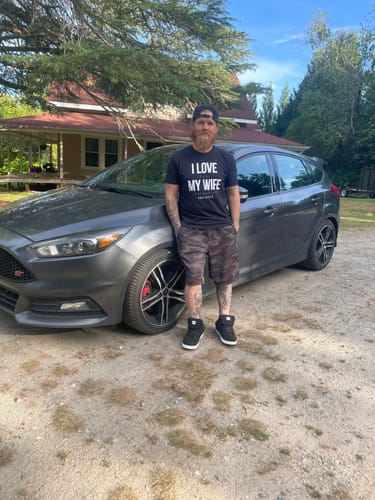 Reviewer wearing the black Love My Wife Shirt while standing next to a car in a driveway.