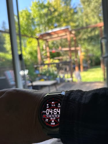 Close-up of a reviewer's smartwatch, showing a digital face with health metrics and 74% battery.