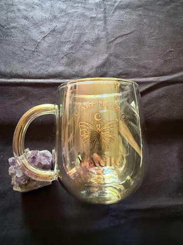 Kunde zeigt die leere, schimmernde Magische Glas-Tasse auf einem dunklen Tuch.