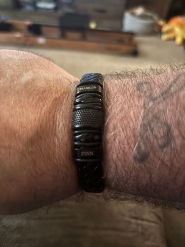 Close-up of a customer's wrist wearing the personalized black bracelet, with the name 'Finn' visibly engraved on a link.
