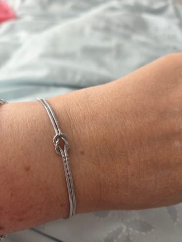 Close-up of a customer's wrist wearing a delicate silver-colored bracelet with a central knot design.