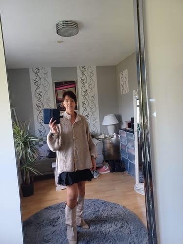 Kundin in einem Spiegel-Selfie, die den beigen 'CozyGlam'-Cardigan und den schwarzen 'Summer'-Rock trägt.