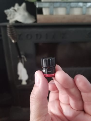 Customer holding a small sample vial of Ember perfume oil in front of a dark wood stove.