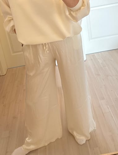 Kundin trägt die lange, weit geschnittene Satin Hose in hellem Cremeweiß.