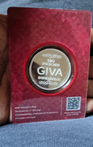 Reviewer holds the Silver Sacred Coin in red packaging, showing the back of the coin with brand and weight details.