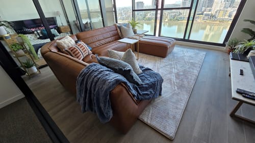 Customer's Desert Mosaic Mellow Mat in a modern living room, with a brown sectional sofa placed on it.