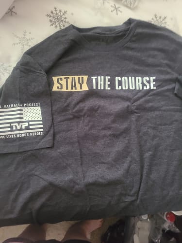 Customer displays a dark grey T.V.P. shirt with 'STAY THE COURSE' on the front, received from their monthly membership.