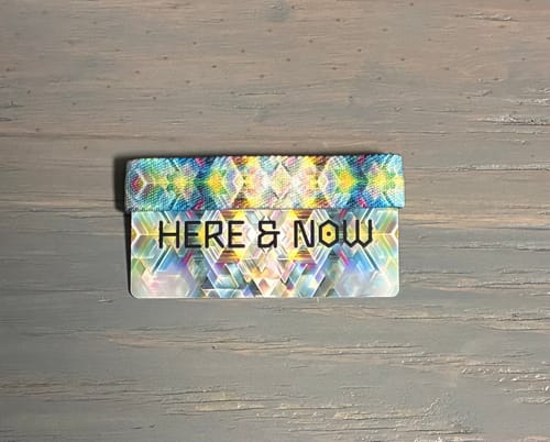 Customer's colorful Here & Now Bracelet on its prismatic packaging card against a gray surface.