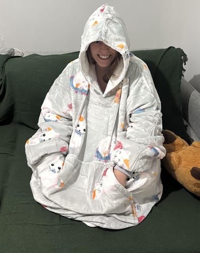 Cliente sorri em um sofá, vestindo o confortável e grande cobertor Sleepo Gatinho.
