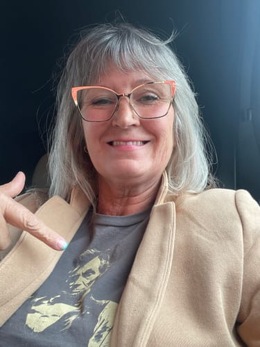 Reviewer smiling and pointing to the detailed print on her grey Lincoln Guitar T-Shirt.