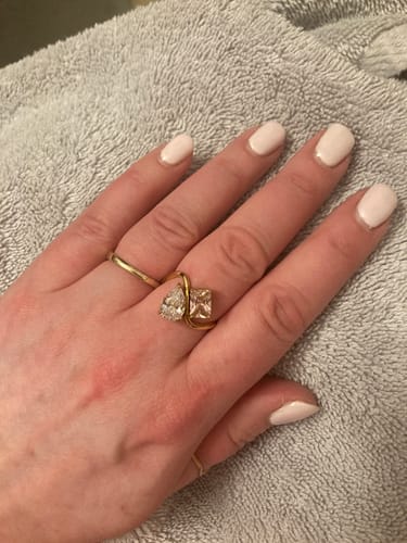 Customer's hand wearing the Navae Birthstone Ring, showing its two distinct pear and radiant-cut stones on a flowing gold band.