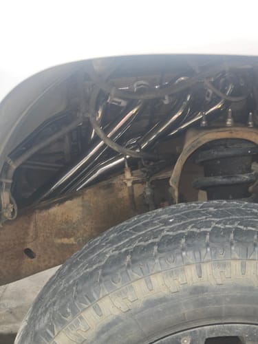 Reviewer's view of the shiny Long Tube Headers installed inside the wheel well of their truck.