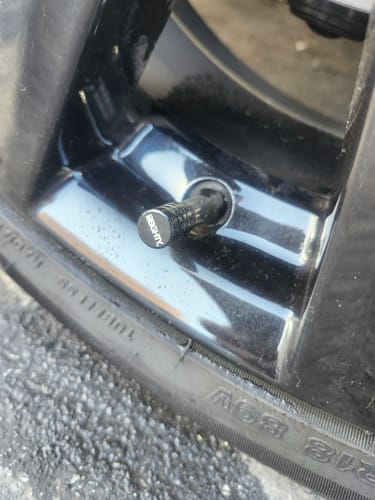 Close-up of a customer's black 80Eighty Valve Stem Cap installed on a glossy black car wheel.