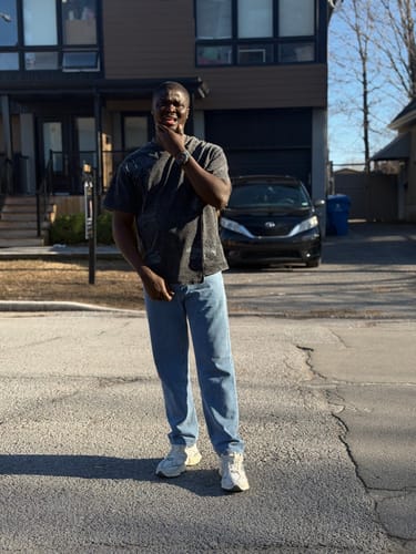 Customer poses outdoors wearing the dark Suede Logo Embroidered Patchwork T-Shirt with jeans.