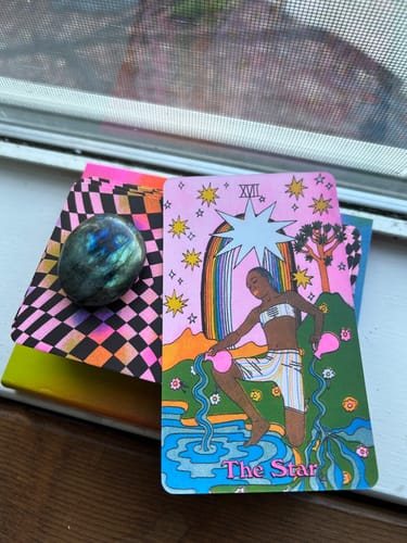 Reviewer's iridescent Labradorite Moonstone from their crystal subscription placed next to a colorful tarot card.
