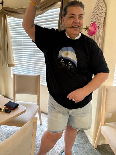 Reviewer happily posing in the black Statement Made Argentinian t-shirt while holding a pink rose in their mouth.