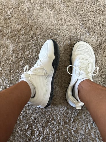 Customer's top-down view wearing the white City Wide Toe Box shoes with black soles on a carpet.