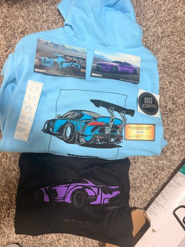 Reviewer's black 80Eighty DCG88 Shirt with a purple car graphic, shown with a blue hoodie and stickers from the brand.