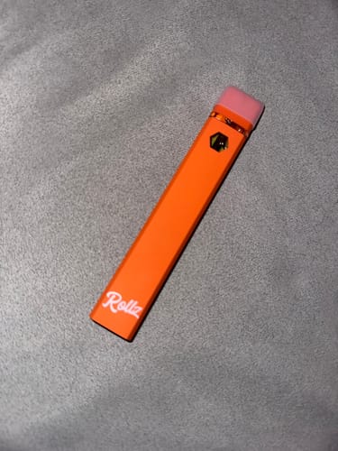 Customer's orange ROLLZ THCA Vape with a pink cap, shown on a grey fabric surface.