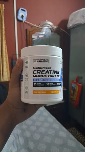 Reviewer's hand holding a white tub of Wellcore Micronised Creatine Monohydrate in Tropical Tango flavor.