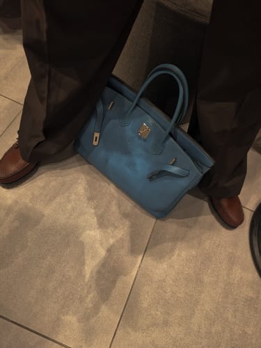 Customer photo of a blue handbag on a floor, edited with the Boujee preset for a dark, moody look.