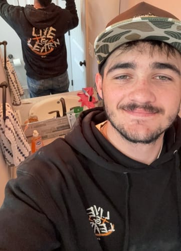 Reviewer takes a mirror selfie to display the front and back of the black LIVE & LEARN HOODIE.