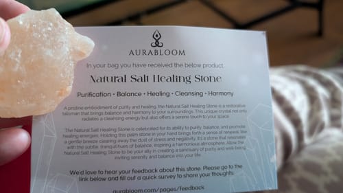 A customer holds a pink salt healing stone next to the descriptive card included in their VIP Crystal Club box.