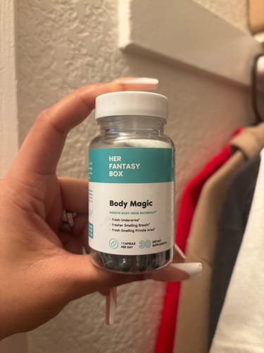 Reviewer's hand holding a clear bottle of Body Magic Chlorophyll Pills, showing the dark capsules inside.