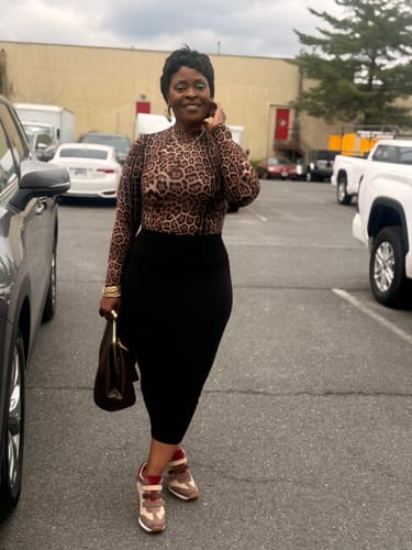Customer wearing the black NW Midi Skirt with a leopard print top and sneakers in a parking lot.