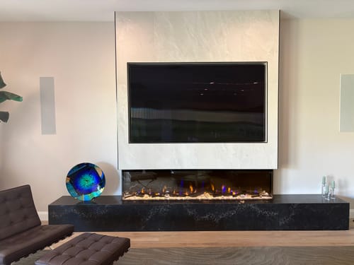 Customer's Dimplex IgniteXL Bold fireplace installed in a stylish media wall below a TV, set within a black marble hearth.
