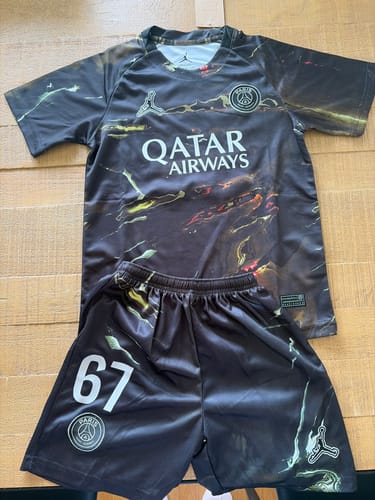 Avis d'un client : L'ensemble enfant PSG Night Edition, avec maillot et short à motifs sombres, est posé à plat.