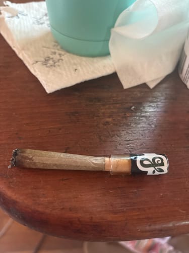 Customer's White Runtz Pre-Roll with a glass mouthpiece, partially smoked and resting on a wooden table.