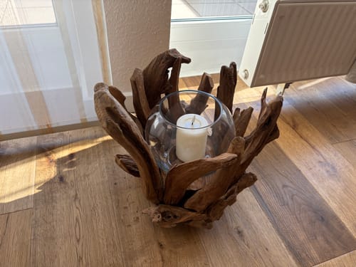 Kunde zeigt den VONDRO Wurzel Kerzenständer mit einer Kerze darin auf einem Holzboden.