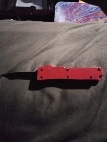 Customer's red Mamba Micro OTF knife with its black blade extended, lying on a dark fabric surface.