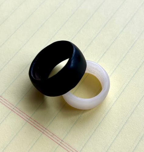 Customer's two finished rings from the craft kit, one dark and one light, linked together on a table.