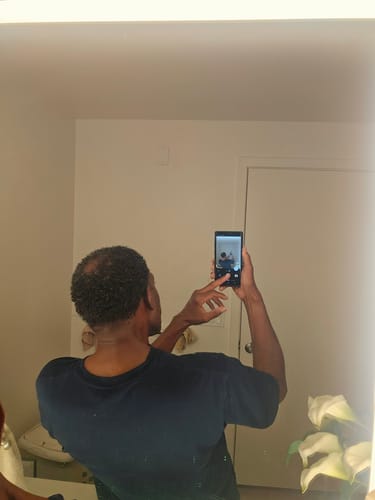 Customer's photo in a mirror showing thinning hair on the crown of their head before using the serum.