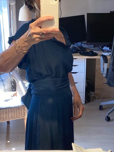 Cliente portant la robe Acacia bleu foncé, ceinturée à la taille avec des manches à volants.